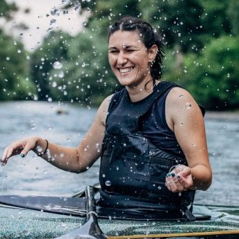 Lachende Frau im Kanu umgeben von spritzendem Wasser.