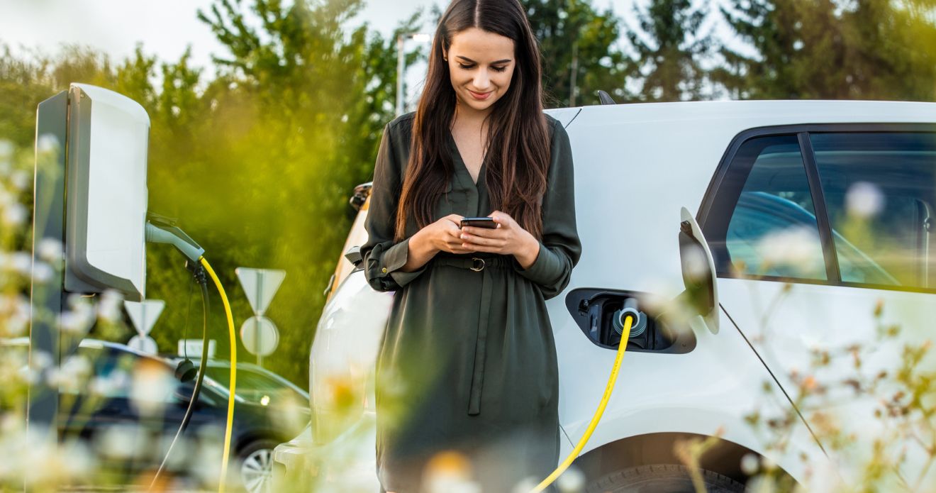 Eine Frau steht neben ihrem Elektroauto, während es lädt.  Eine Frau steht neben ihrem Elektroauto, während es lädt.