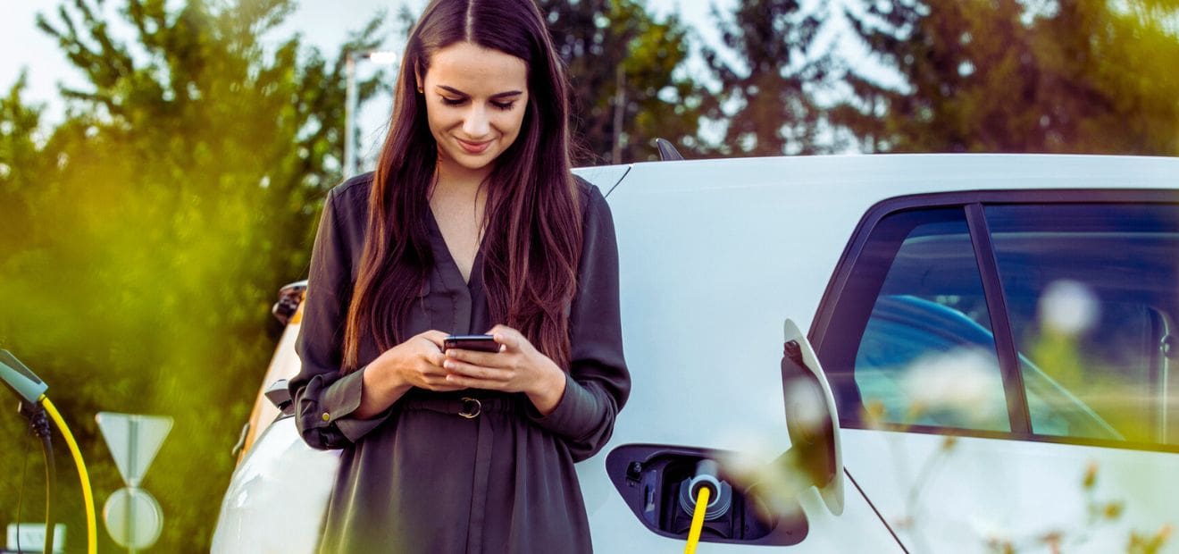 Eine Frau steht neben ihrem Elektroauto. Jezt zur günstigen Kfz-Versicherung für E-Autos.