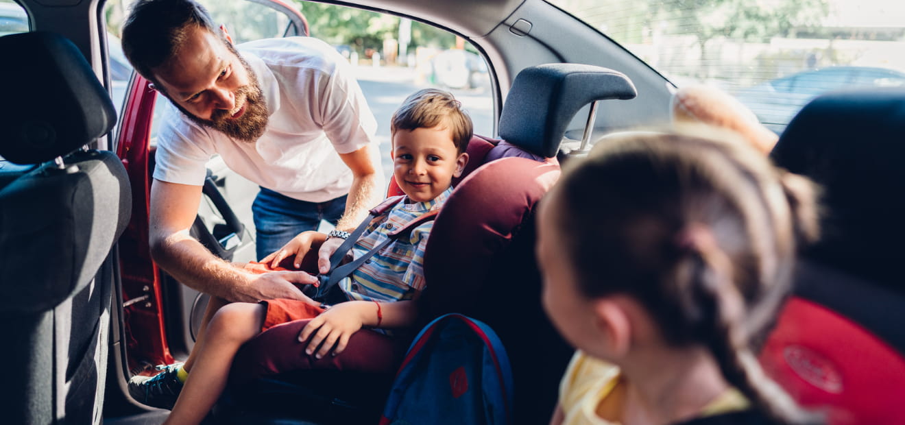 Ein Mann schnallt ein Kinder im Kindersitz an. 