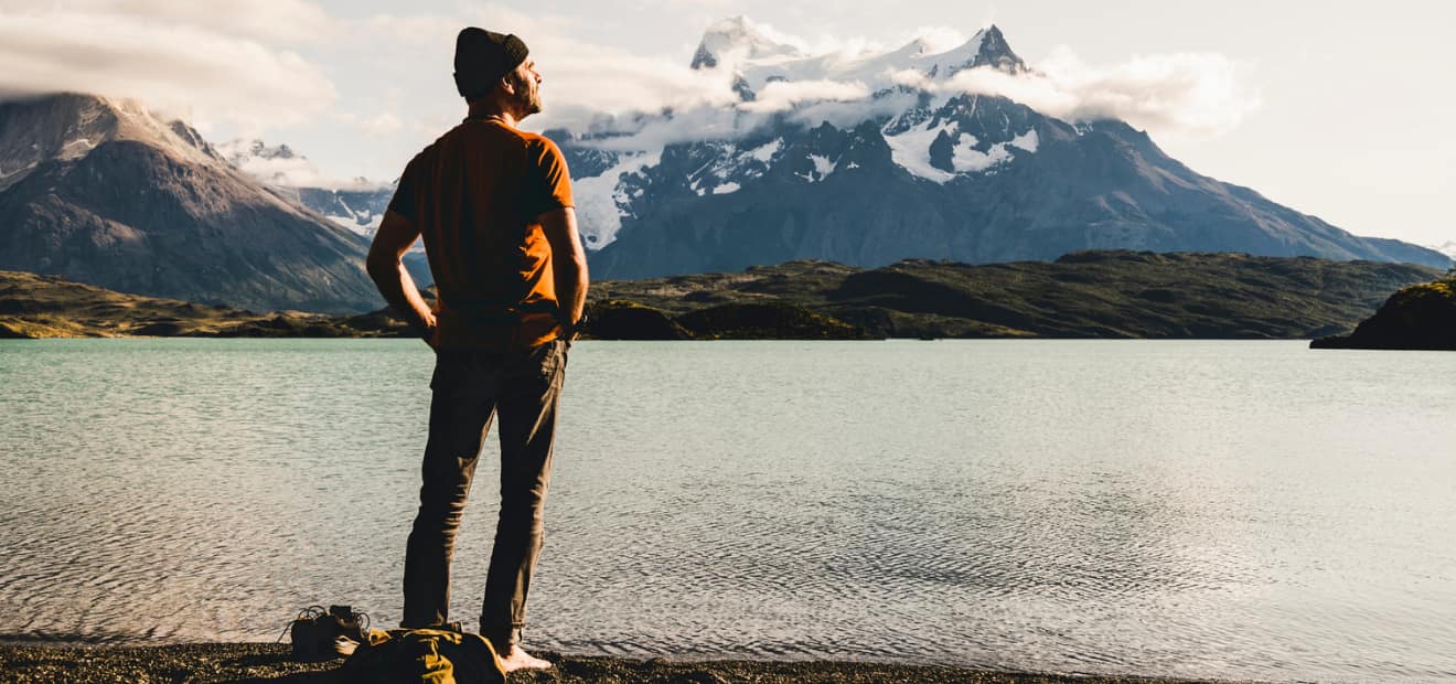 Ein Mann steht vor einem See und genießt die Aussicht auf eine Bergkette.