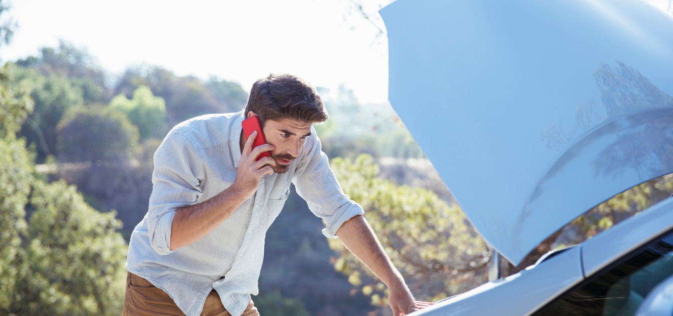Ein Mann betrachtet den Motorraum seines Autos und telefoniert. 
