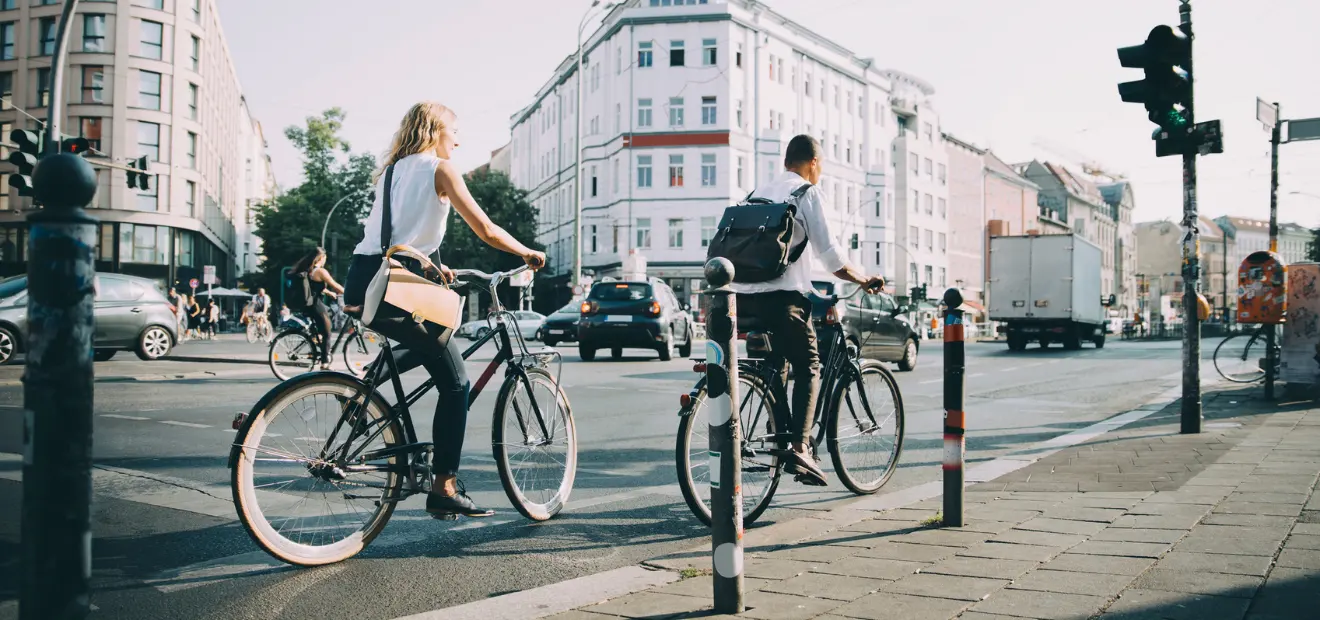 Eine Frau und ein Mann fahren auf einer stark befahrenen Kreuzung mit dem Fahrrad. 