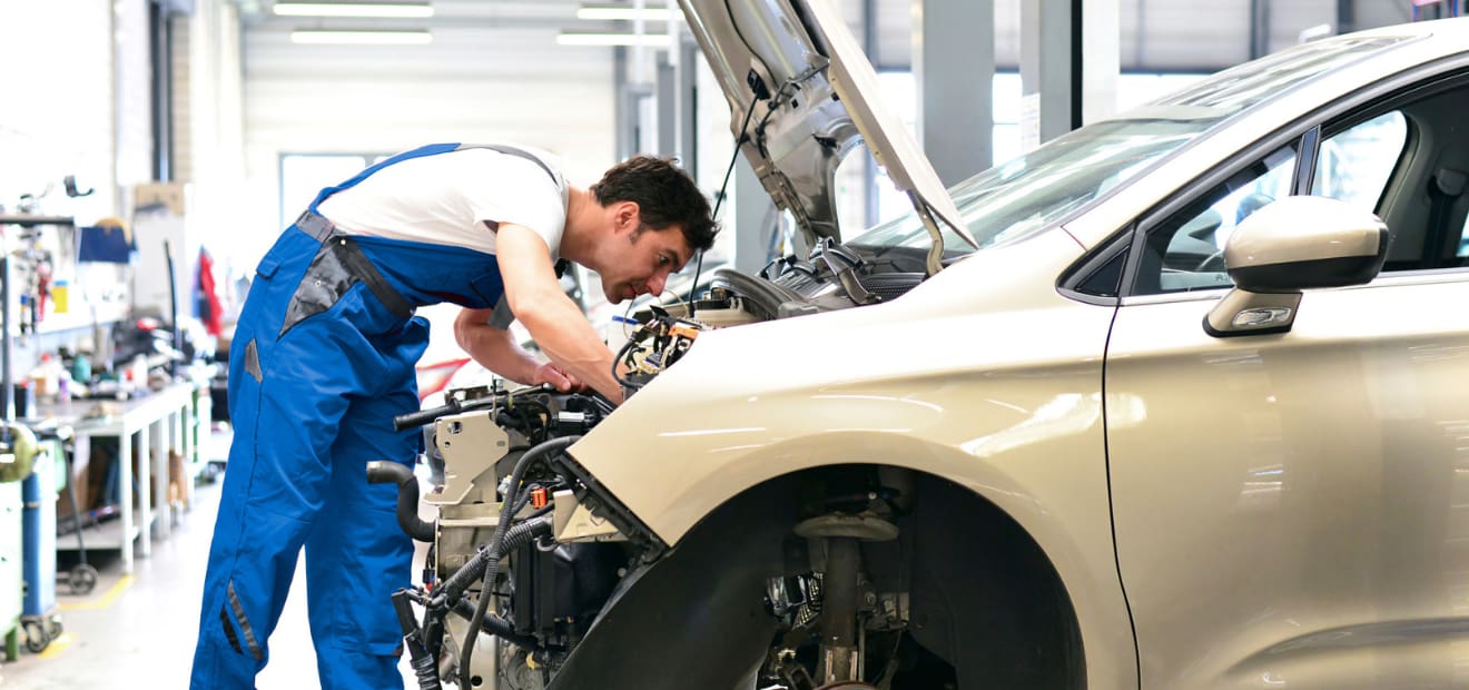 Ein Mechaniker arbeitet im Motorraum eines Autos. 