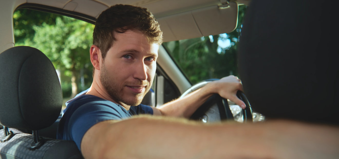 EIn Mann sitzt am Steuer seines Autos und schaut zufrieden nach hinten über seine Schulter. Jetzt Kfz-Versicherung von AdmiralDirekt abschließen!