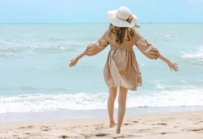 Frau mit Sommerkleid und Hut am Meer.