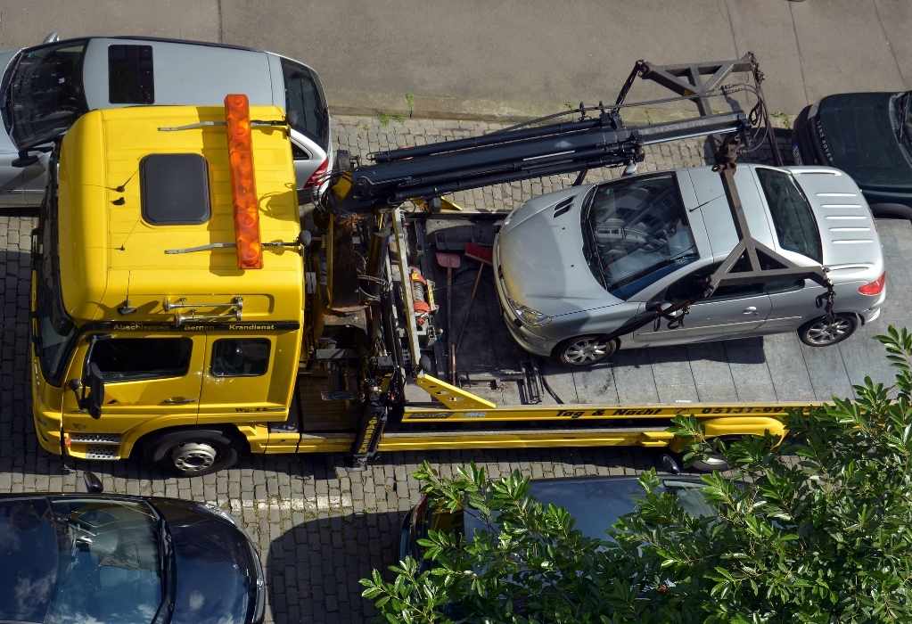 Ein gelber Abschleppwagen mit Krahn hebt ein Auto auf die Ladefläche.