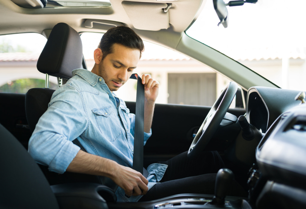 Ein Mann in einem Auto schnallt sich an. 