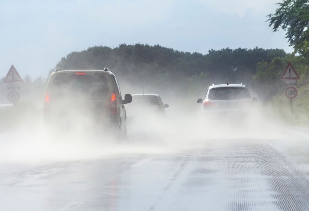 Mehrere Autos fahren auf einer nassen zweispurigen Straße. Das linke Fahrzeug bremst. 