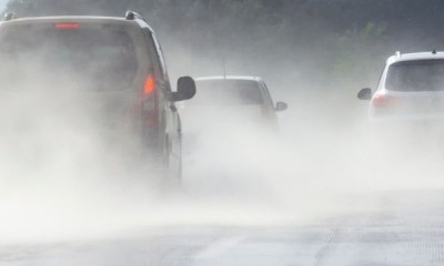 Mehrere Autos fahren auf einer nassen zweispurigen Straße. Das linke Fahrzeug bremst. 