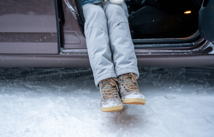 Eine Person sitzt in der geöffneten Autotür und klopft den Schnee von ihren Stiefeln.
