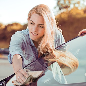 Eine junge Frau poliert ihr Auto auf Hochglanz.