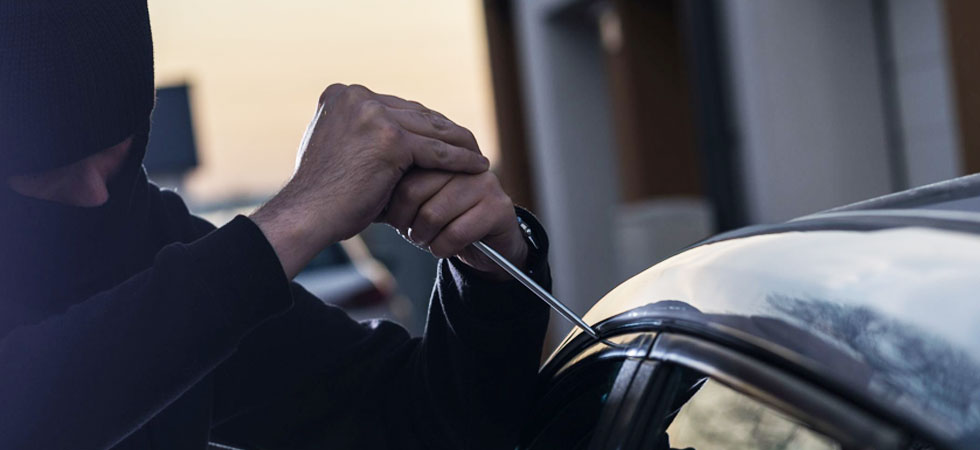 Ein Autodieb versucht eine Scheibe aufzuhebeln.