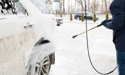 Ein Mann wäscht im Winter ein verschneites Auto mit einem Hochdruckreiniger in einer Waschanlage.