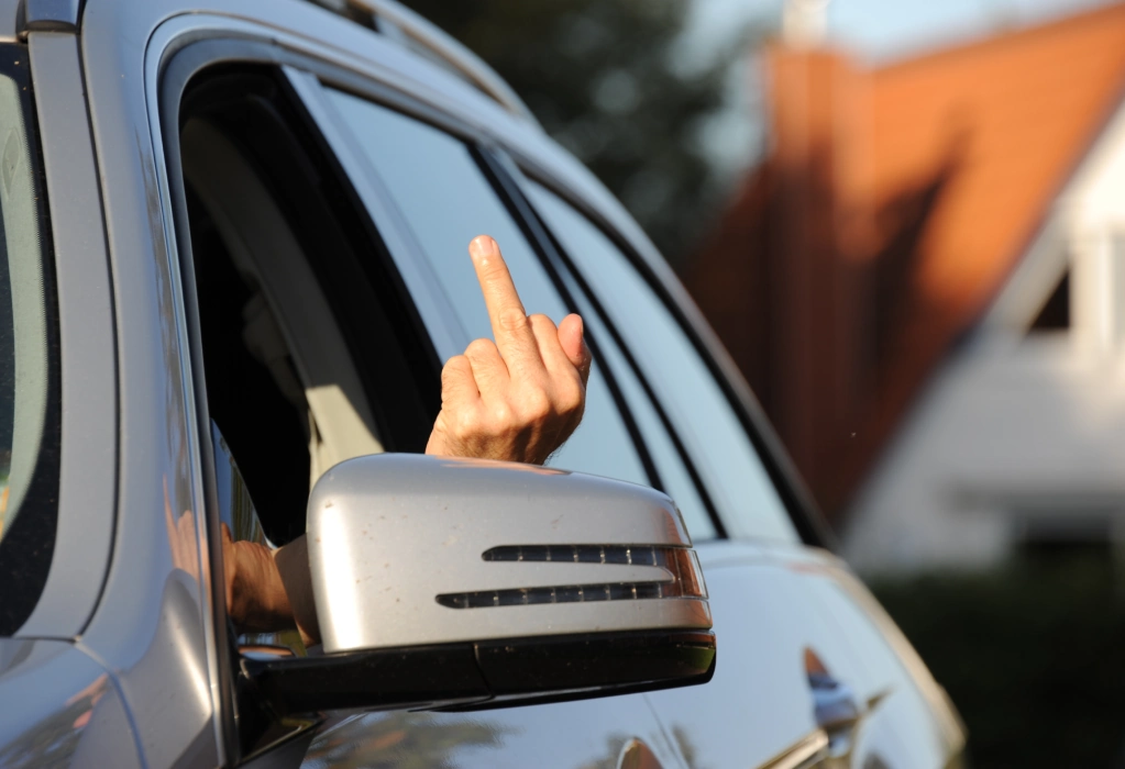 Eine Person streckt aus dem Fenster eines Autos den Mittelfinger als beleidigende Geste heraus.