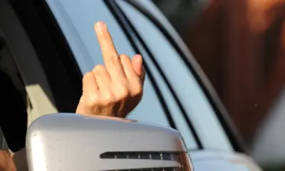 Eine Person streckt aus dem Fenster eines Autos den Mittelfinger als beleidigende Geste heraus.