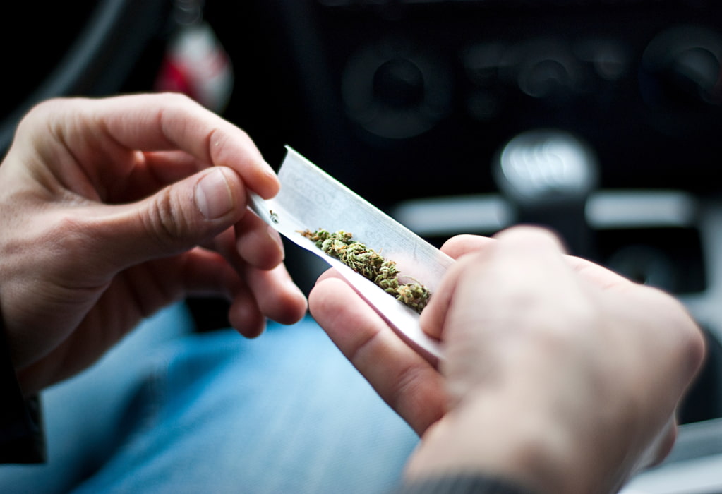 Ein Mann dreht einen Joint in einem Auto. 