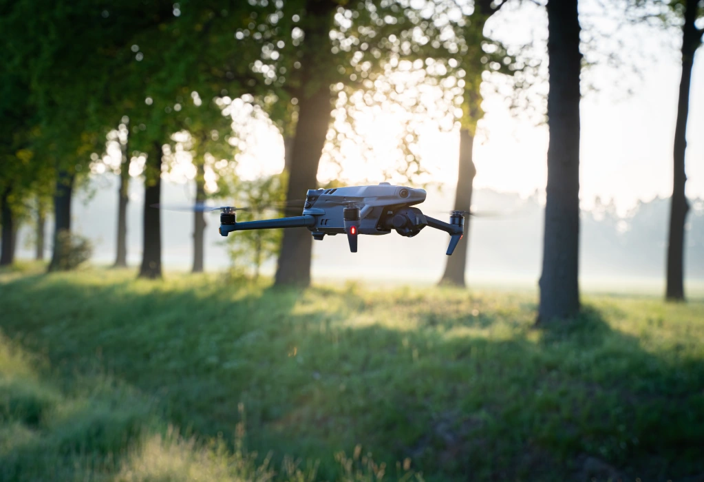 Eine Drohne fliegt in geringer Höhe über einer Wiese an Bäumen vorbei bei Sonnenaufgang.