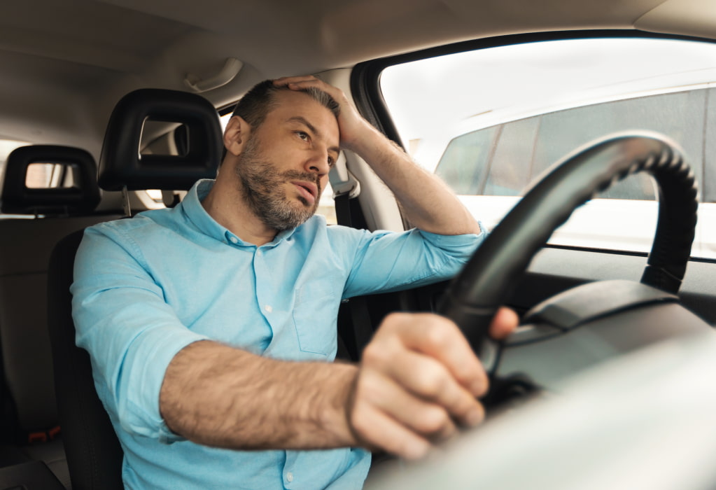 Ein Mann sitzt im Auto und rauft sich genervt die Haare.