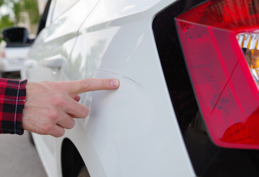 Hand zeigt auf einen Kratzer im Auto-Lack
