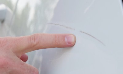 Hand zeigt auf einen Kratzer im Auto-Lack