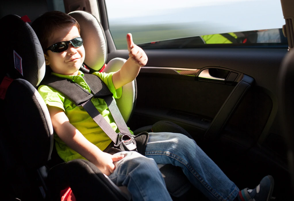 Kleiner Junge mit Sonnenbrille sitzt im Auto und zeigt seinen Daumen nach oben.