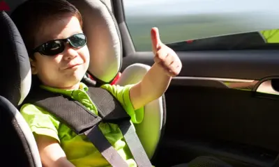 Kleiner Junge mit Sonnenbrille sitzt im Auto und zeigt seinen Daumen nach oben.