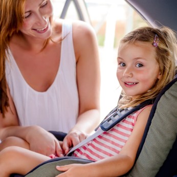 Frau schnallt ein Kind im Kindersitz an. 