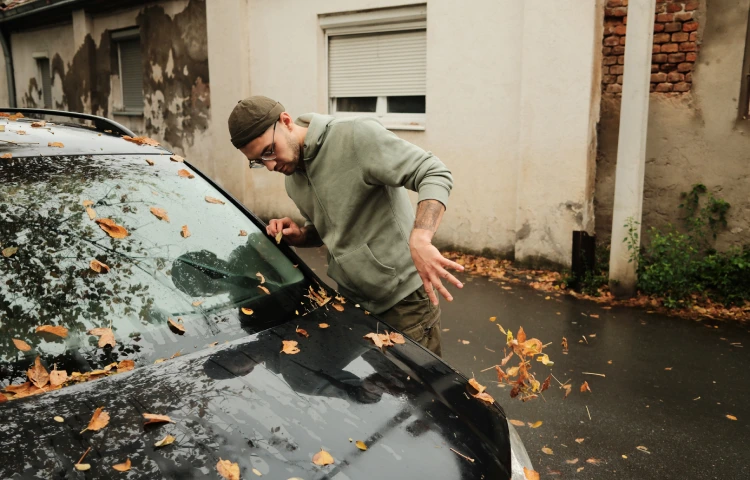 Ein Mann entfernt Laub von der Windschutzscheibe eines Autos. 