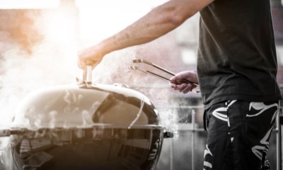 Ein Mann steht vor einem qualmenden Grill auf dem Balkon.