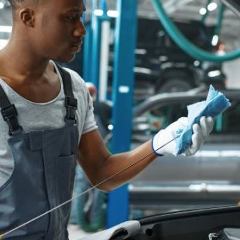 Junger Mann überprüft den Ölstand eines Autos.