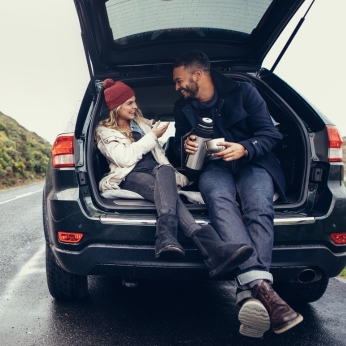 Eine Frau und ein Mann sitzen im Kofferraum und lächeln sich an.