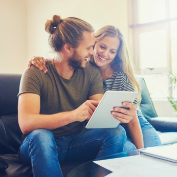 Ein Mann und eine Frau sitzen auf dem Sofa und informieren sich auf dem Tablet-PC über eine Rechtsschutzversicherung.