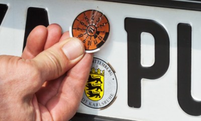 Ein Mann klebt eine neue TÜV-Plakette auf das Kennzeichen eines Autos. 