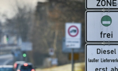 Ein Straßenschild weist auf eine Umweltzone hin, in der nur Fahrzeuge mit grüner Plakette fahren dürfen. Im Hintergrund ist eine Straße mit mehreren Autos zu sehen. 