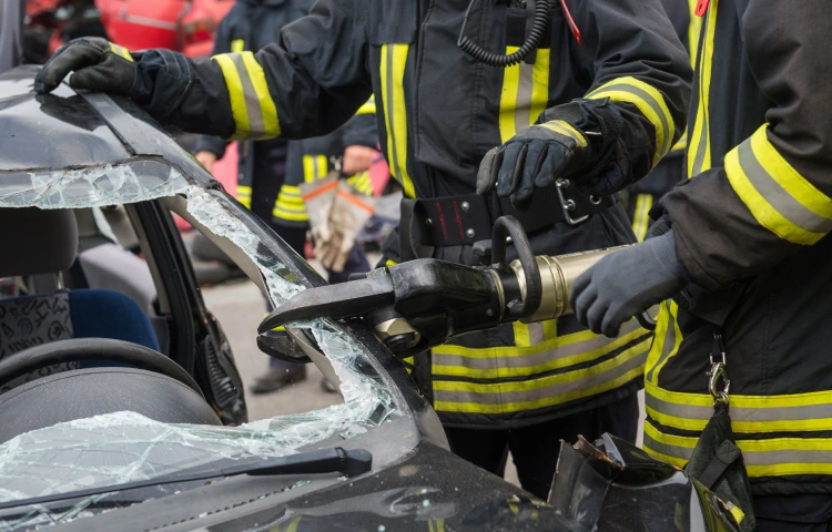 Feuerwehrleute schneiden mit hydraulischem Rettungsgerät das Dach eines verunglückten Autos auf.